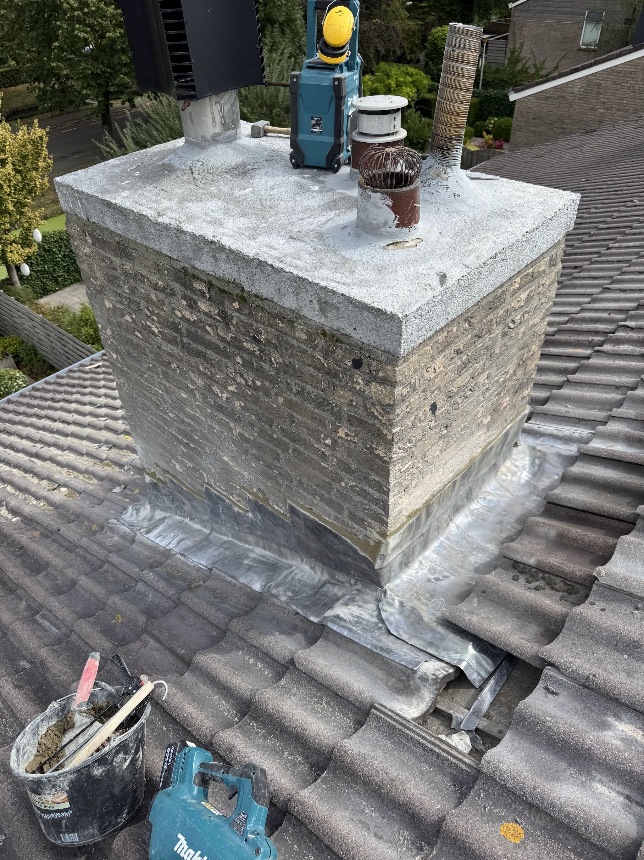 Gemetselde schoorsteen met nieuwe betonnen afdekplaat en nieuw daklood op een pannendak