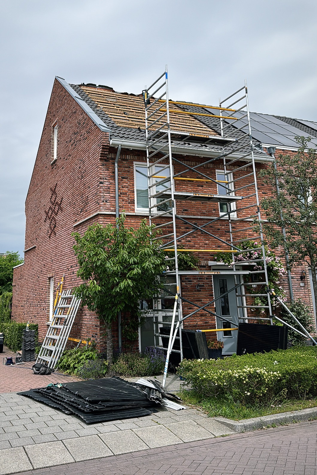 Woning met steiger waar het dak wordt vervangen, de ladders en nieuwe dakplaten staan op de stoep
